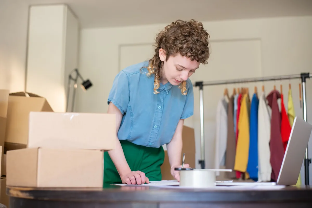 Small online shop owner preparing orders beside boxes and a laptop
